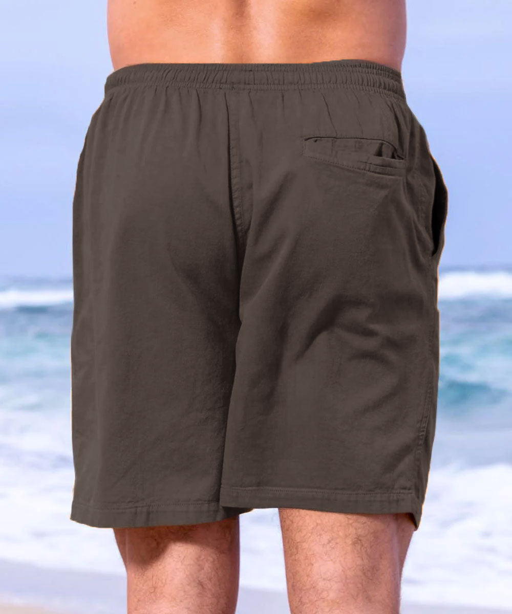 A pair of twill shorts in a brownish-root beer color, with an elastic waistband and drawstring. The shorts are modeled by a person standing on a beach View 3