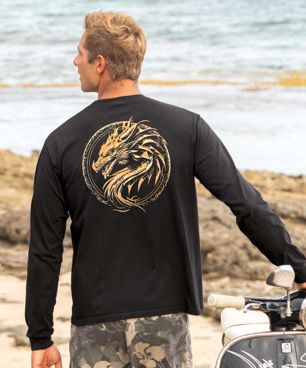 A man standing by the beach wearing a black long sleeve crewneck t-shirt with a gold dragon medallion design on the back. View 2