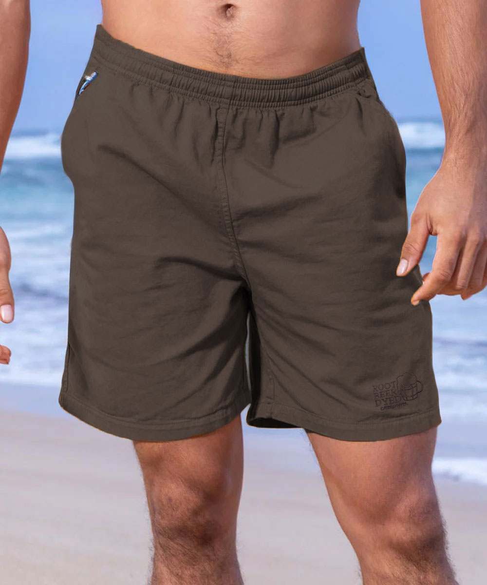 A pair of twill shorts in a brownish-root beer color, with an elastic waistband and drawstring. The shorts are modeled by a person standing on a beach View 2