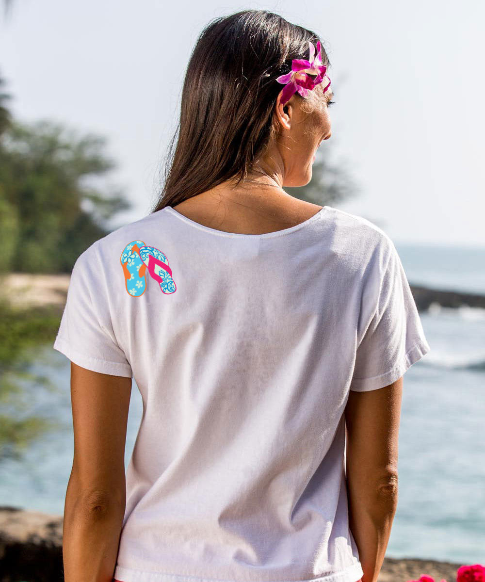 woman standing on the beach wearing a white t-shirt with flip-flops on it. View 3