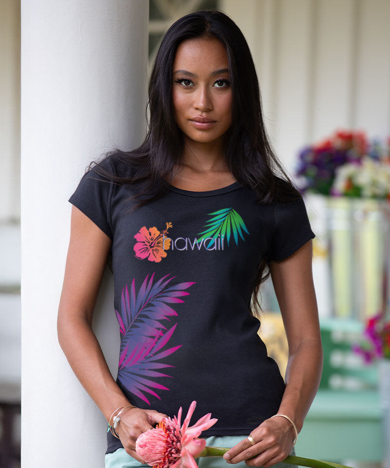Woman wearing a black t-shirt with colorful floral designs and 'Hawaii' text, holding a pink flower. View 2