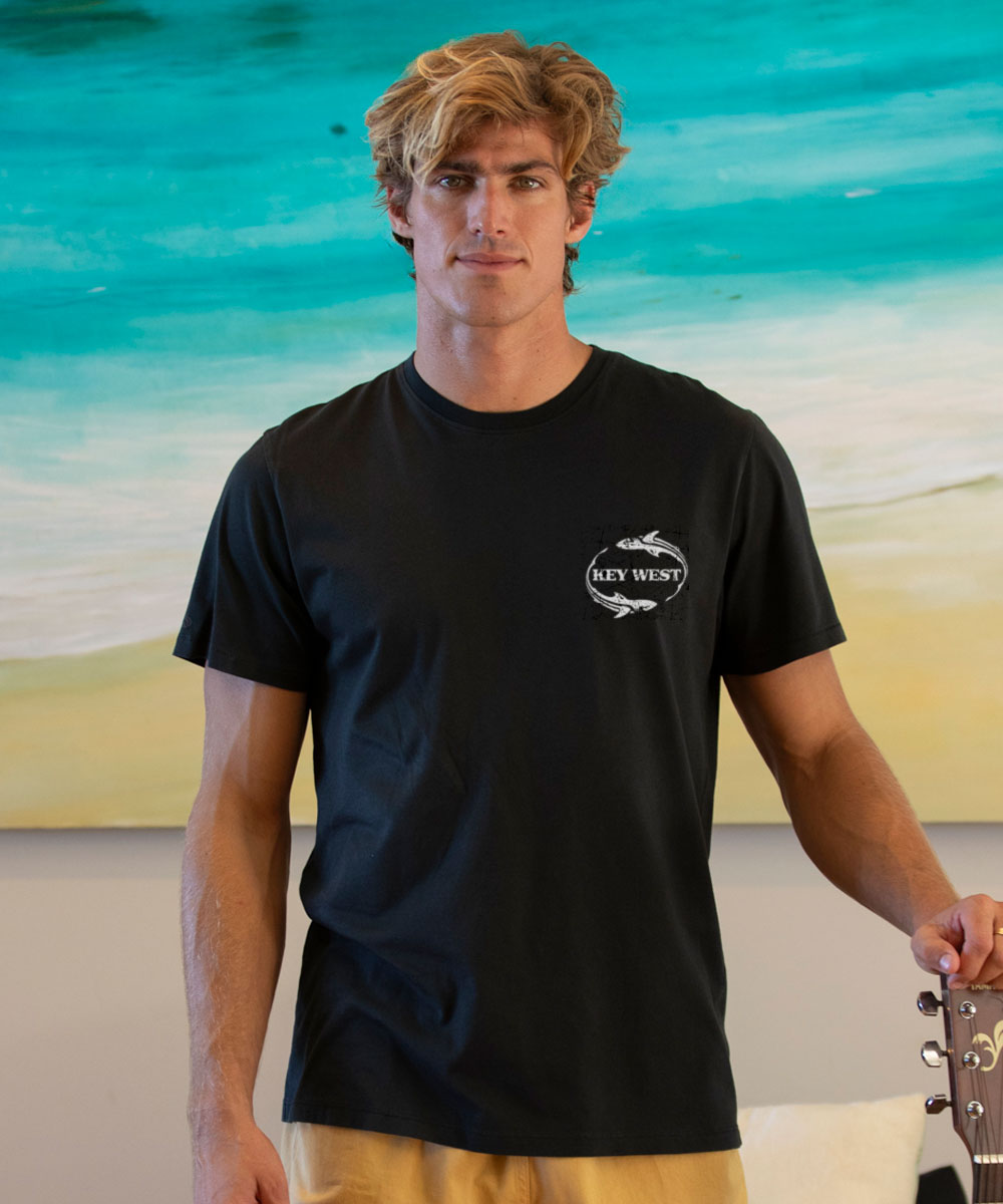 Man wearing a black t-shirt with a logo standing against a beach background View 3