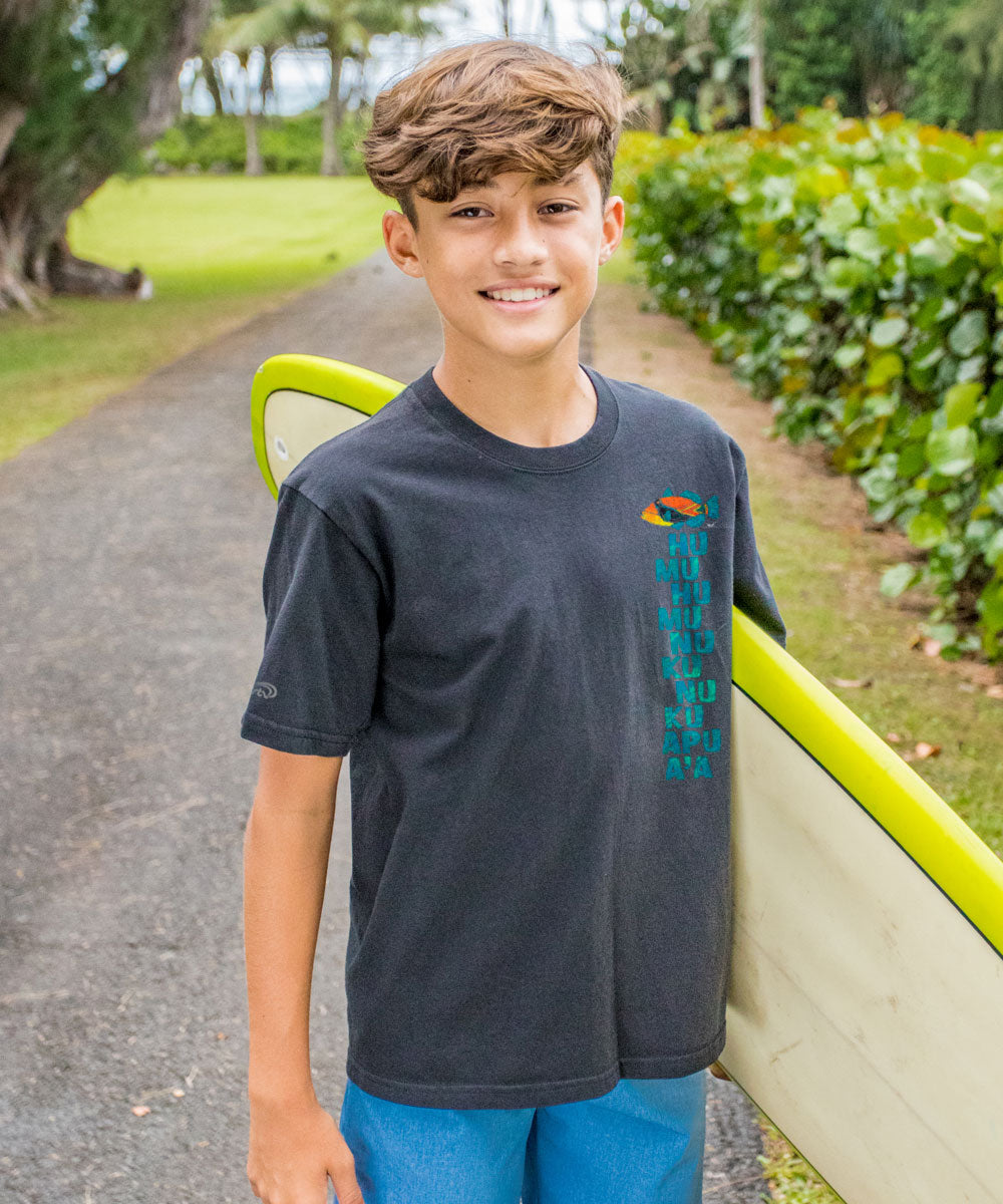 Young boy standing outdoors with a green and yellow object, wearing a dark gray t-shirt with a colorful design. View 3