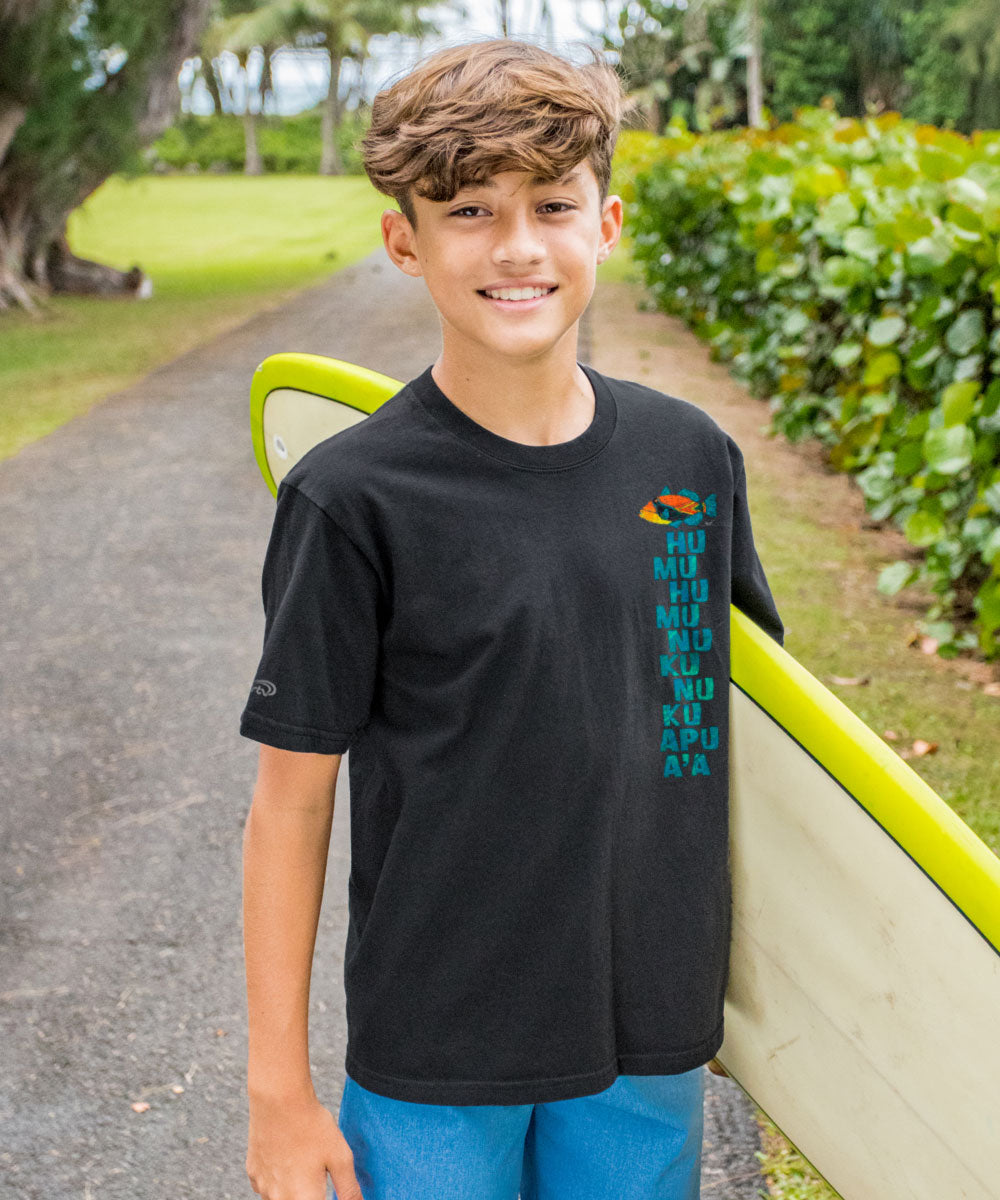 Young boy standing outdoors with a green and yellow object, wearing a dark gray t-shirt with a colorful design. View 3
