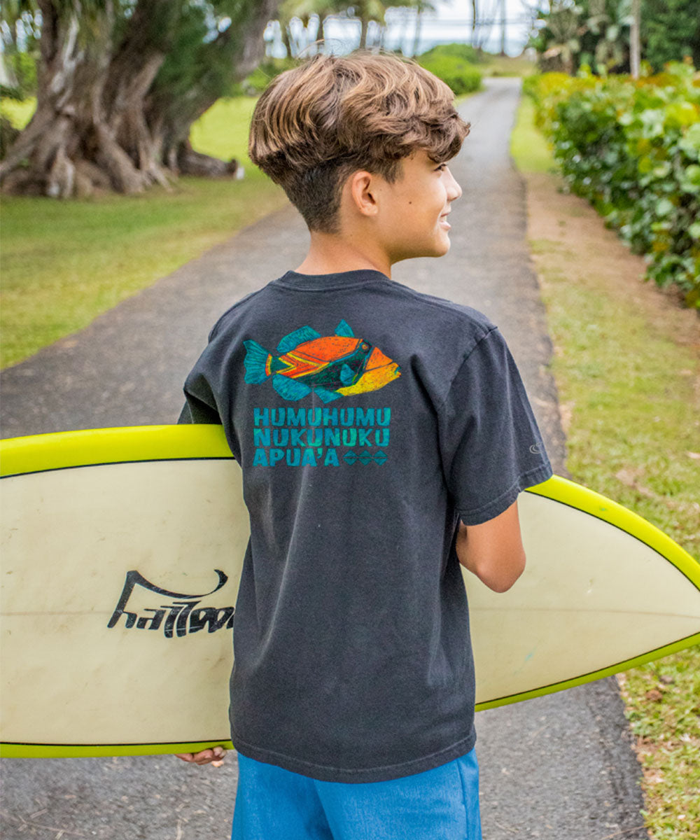 Young boy holding a surfboard with a t-shirt featuring ocean-themed graphics and text. View 2