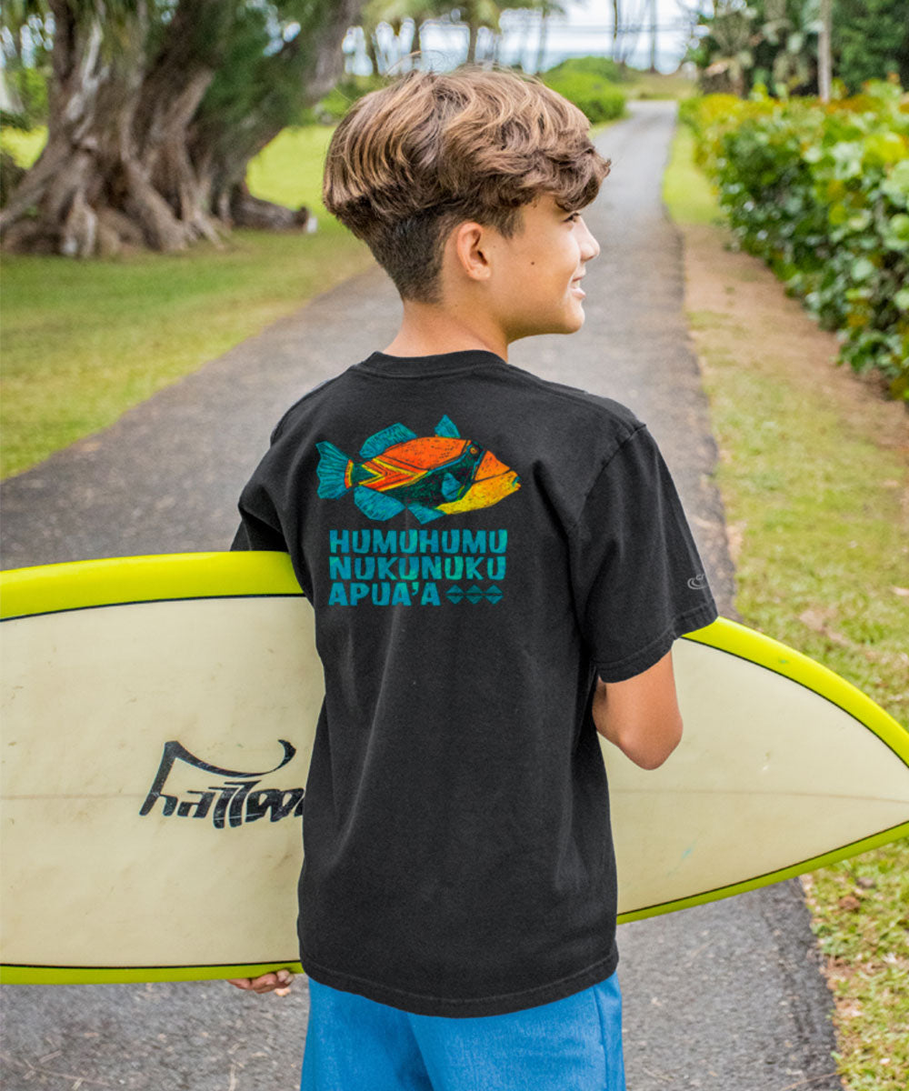 Young boy holding a surfboard with a t-shirt featuring ocean-themed graphics and text. View 2