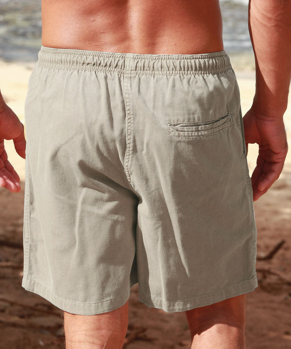 A man wearing light khaki swim trunks, shown from the back on a sandy beach background. View 3