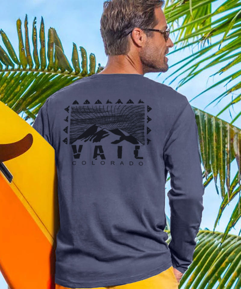 Man wearing a long-sleeve shirt with 'Vail Colorado' text, holding a surfboard with palm trees in the background. View 2