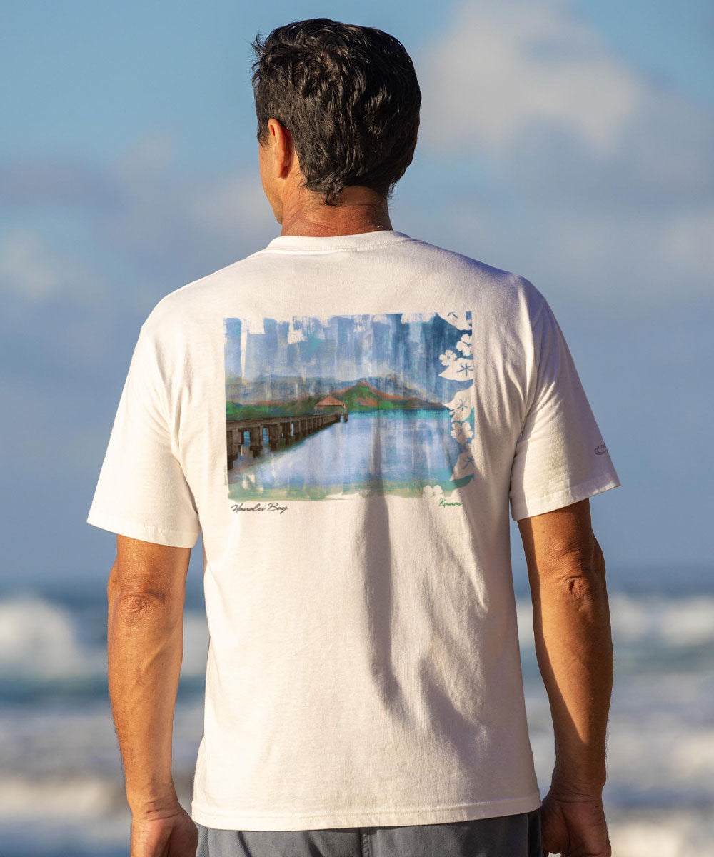 Man wearing a white t-shirt with a scenic print, standing on a beach. View 2