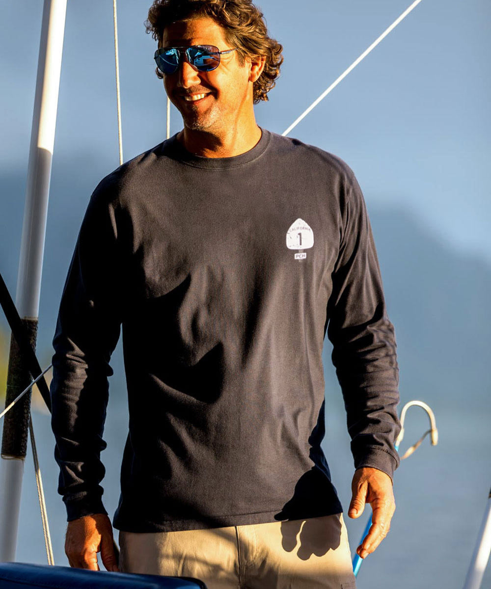A man wearing a black long sleeve crewneck T-shirt with the text 'PACIFIC COAST HIGHWAY' on it, standing near water. View 3