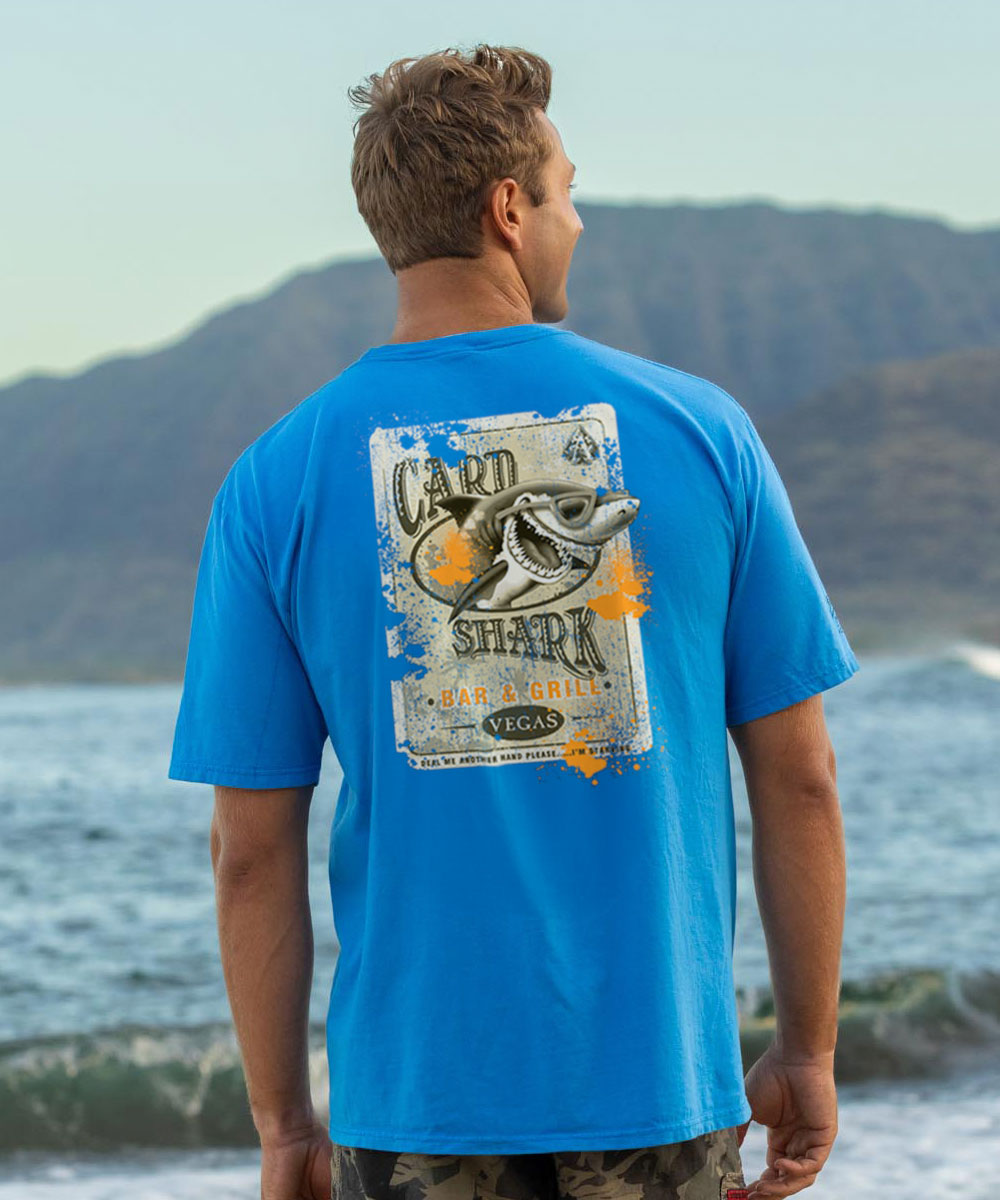 Person wearing a blue t-shirt with a shark graphic on the beach View 2