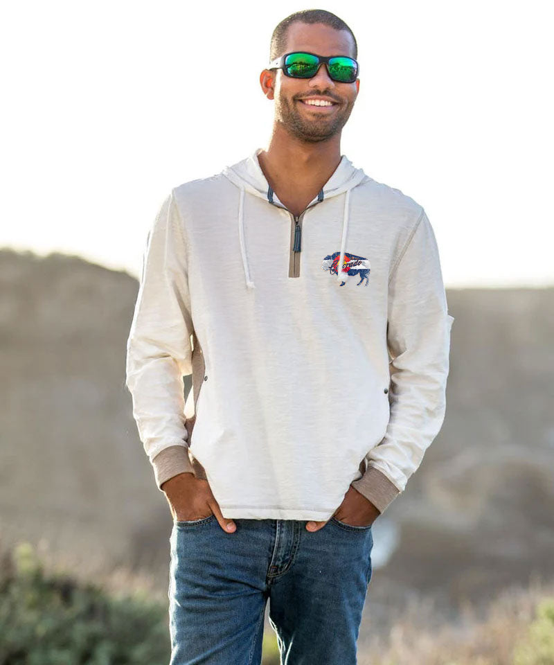Man wearing a light-colored hoodie with a logo, sunglasses, and jeans outdoors. View 3