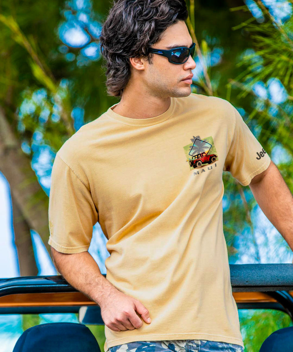 Man wearing a beige t-shirt with a logo, sunglasses, and patterned shorts outdoors. View 3