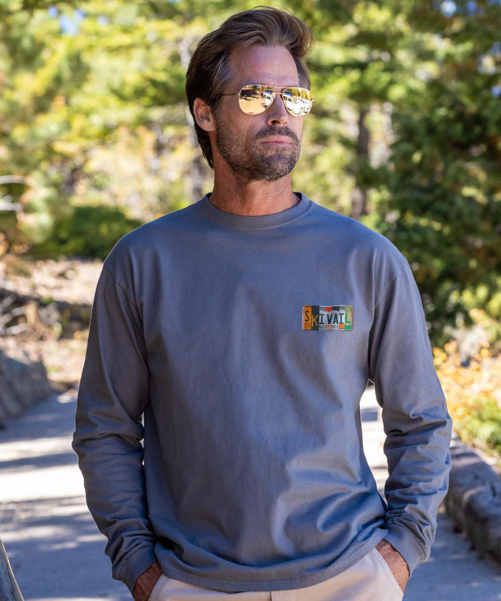 Man wearing a gray long-sleeve shirt with a logo, standing outdoors. View 3