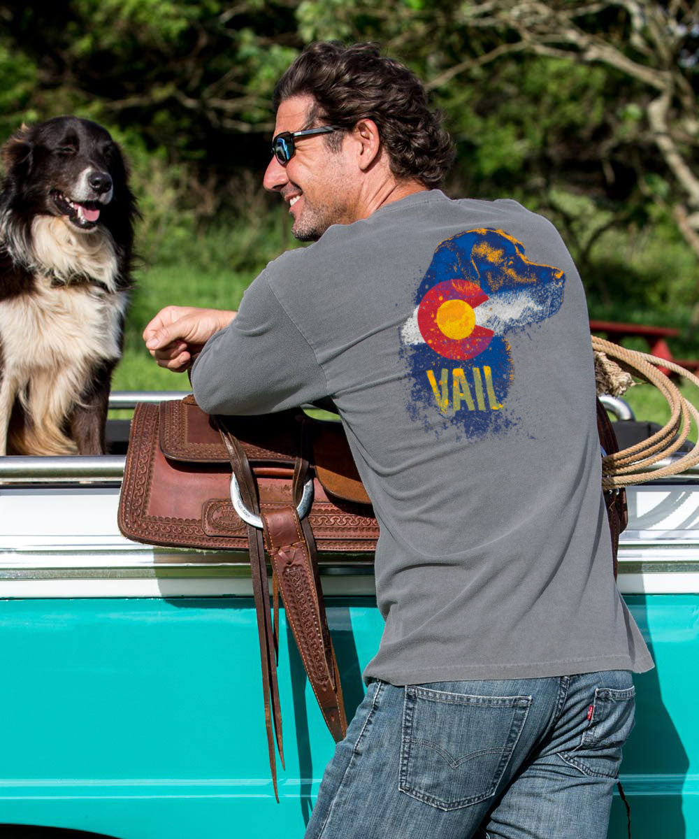 Man with a dog in the back of a turquoise truck, wearing a gray t-shirt with a Colorado design. View 2
