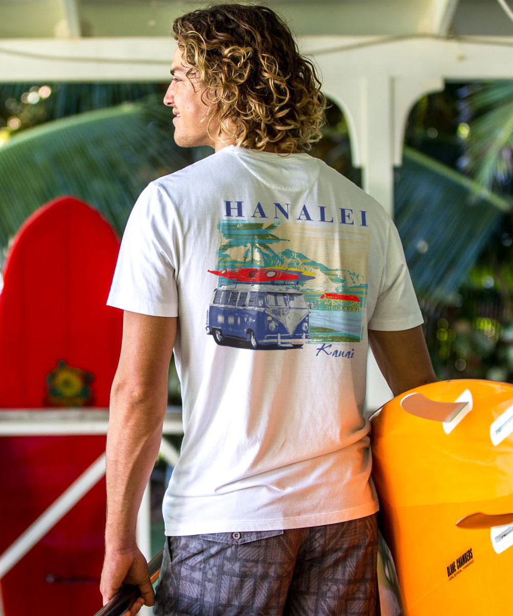 Person wearing a 'Hanalei' t-shirt with a graphic design, standing next to a yellow surfboard. View 2