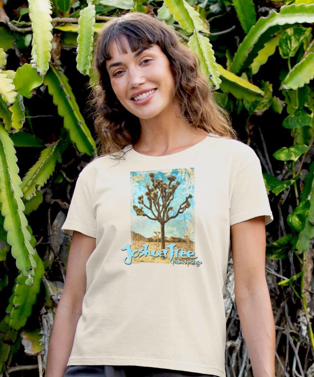Woman wearing a white t-shirt with a Joshua Tree design, standing in front of green plants. View 2