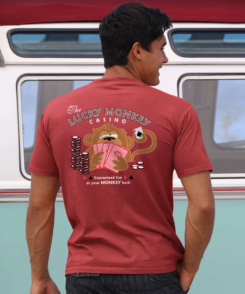 Man wearing a maroon t-shirt with 'Lucky Monkey Casino' design, standing in front of a vintage van. View 2