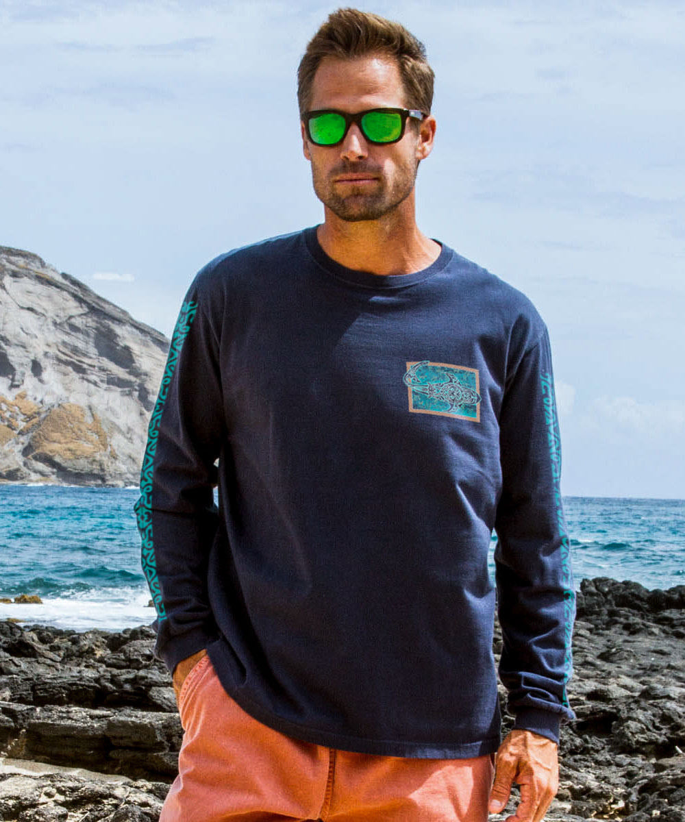 Man wearing sunglasses and a navy blue shirt with a pocket design on a rocky beach. View 3