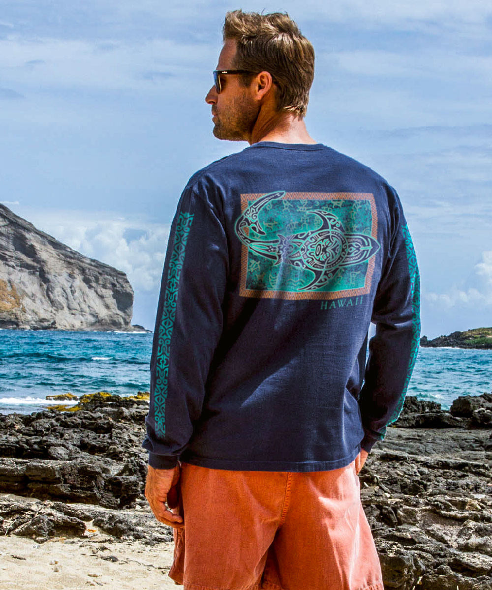 Man wearing a blue shirt with a graphic on the back, standing on a rocky beach. View 2