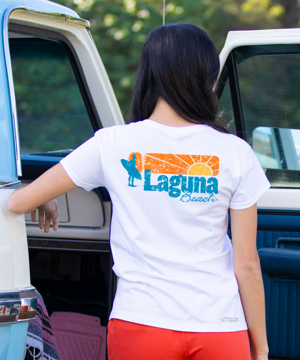 Person wearing a white t-shirt with 'Laguna Beach' design, standing next to a vintage car. View 2
