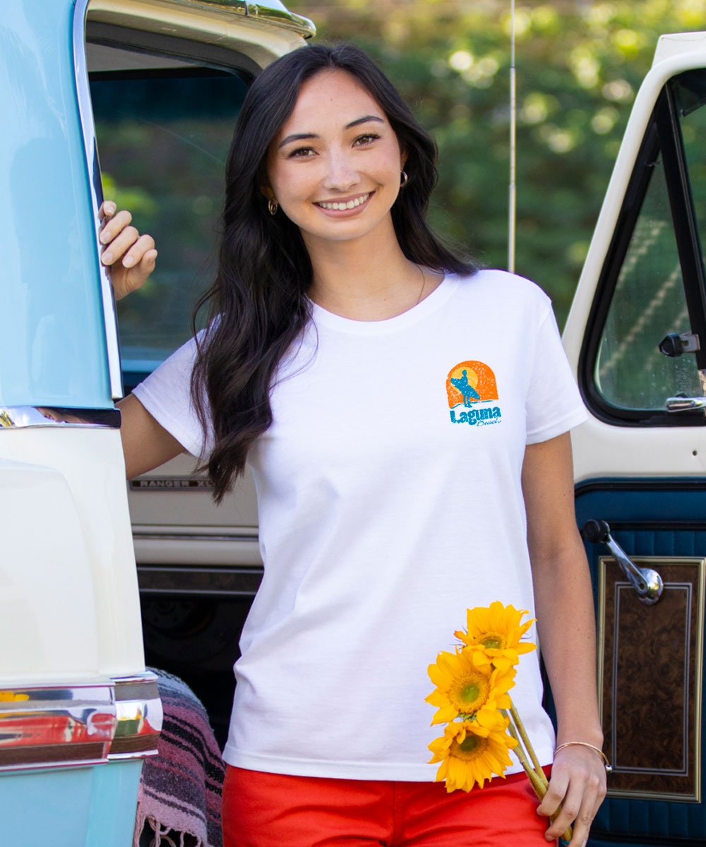 Woman in a white t-shirt with a logo, holding sunflowers, standing next to a vintage van. View 3