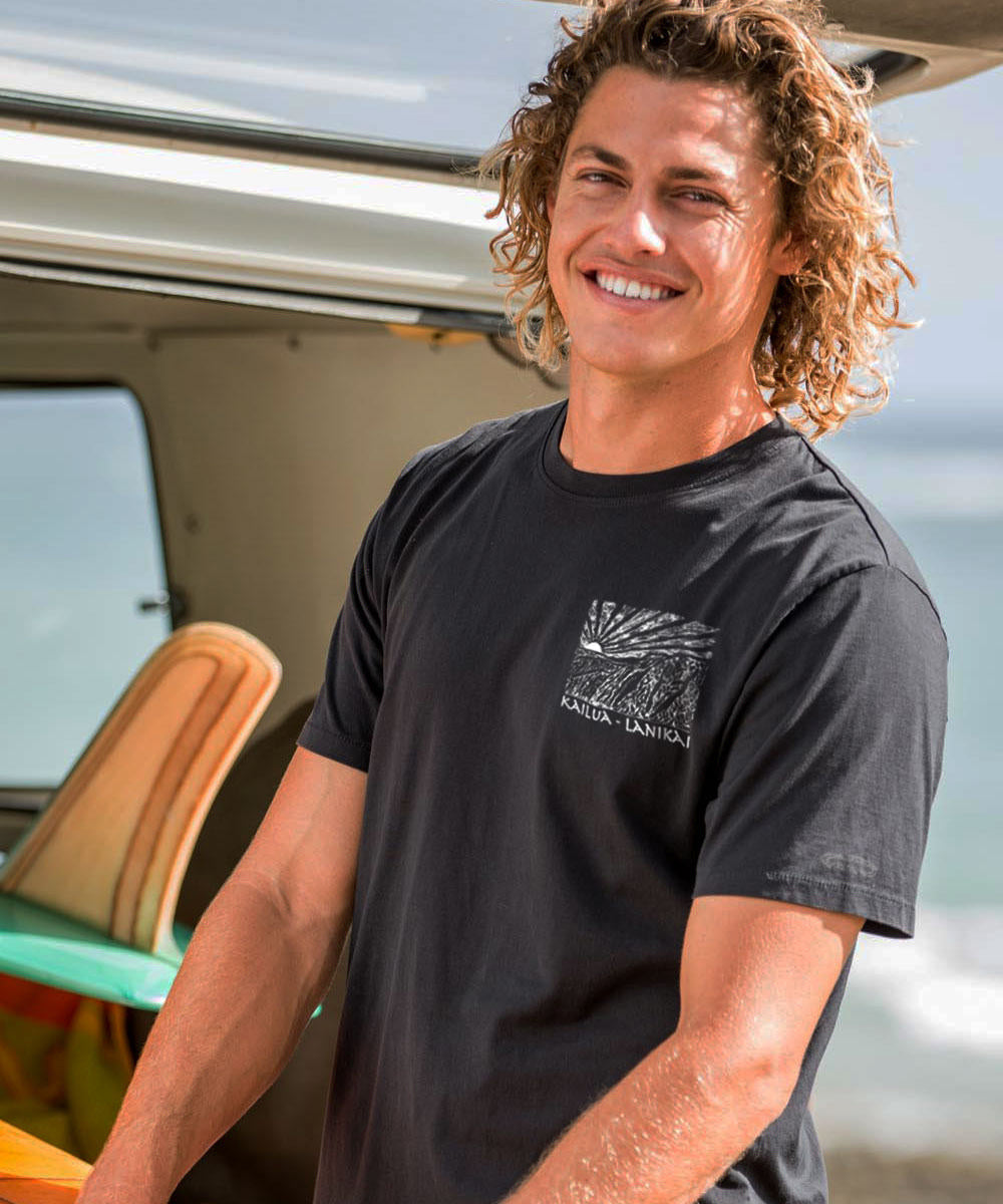 Person with curly hair wearing a black t-shirt by a vehicle outdoors. View 3