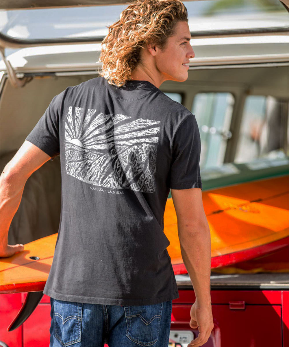 Person wearing a black t-shirt with a graphic design, standing next to a red vehicle with a surfboard. View 2
