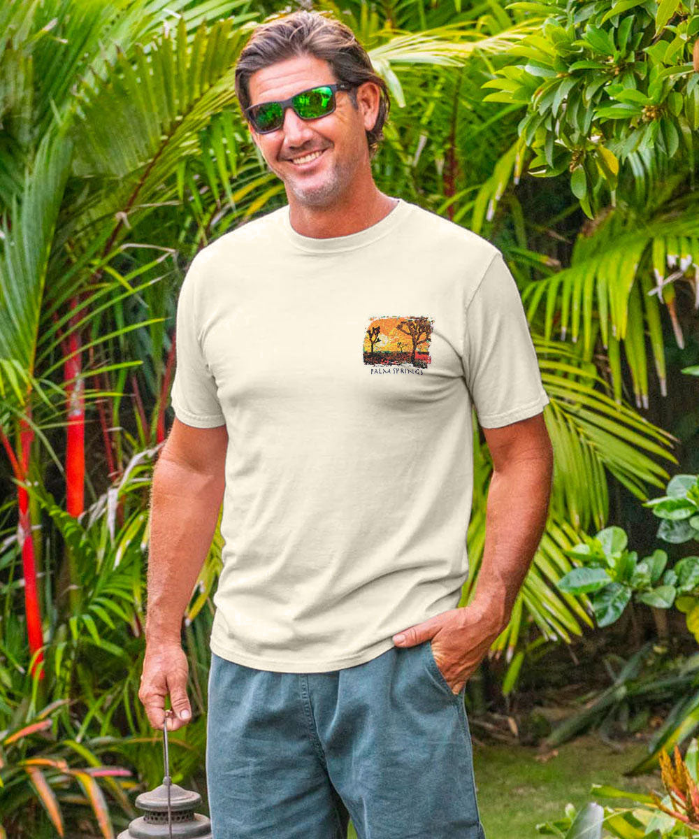 Man wearing a white t-shirt with a graphic design, standing in a lush garden. View 3