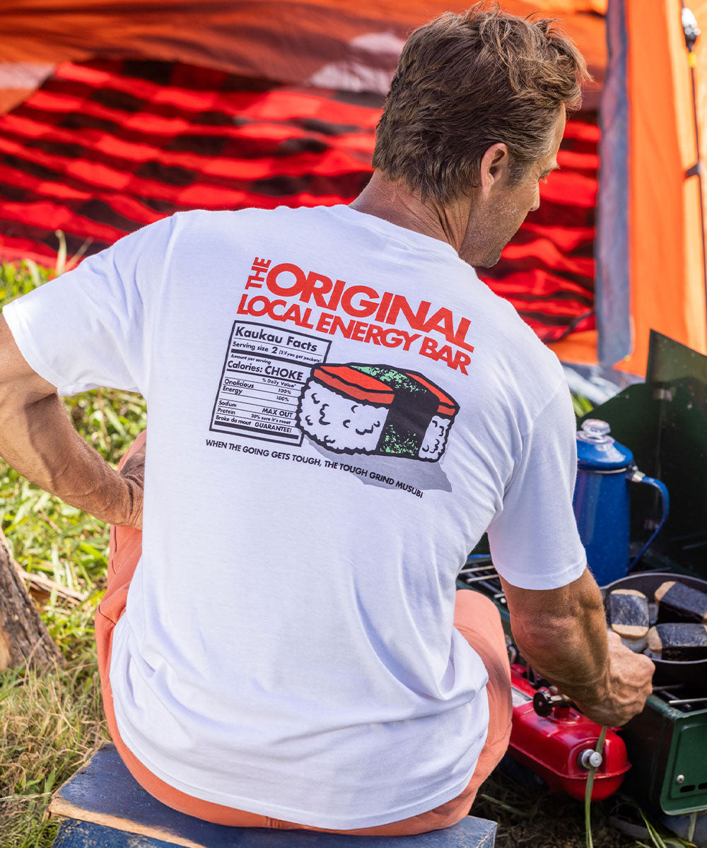 Man wearing a white shirt with a graphic design on it sitting in front of a tent cooking food View 2