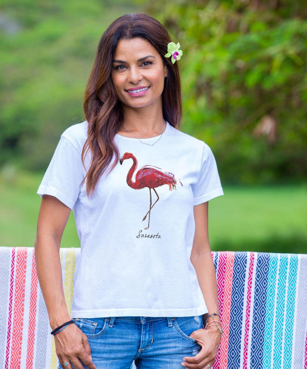 A woman wearing a white short sleeve scoop neck t-shirt with a pink flamingo design, paired with blue jeans. View 2