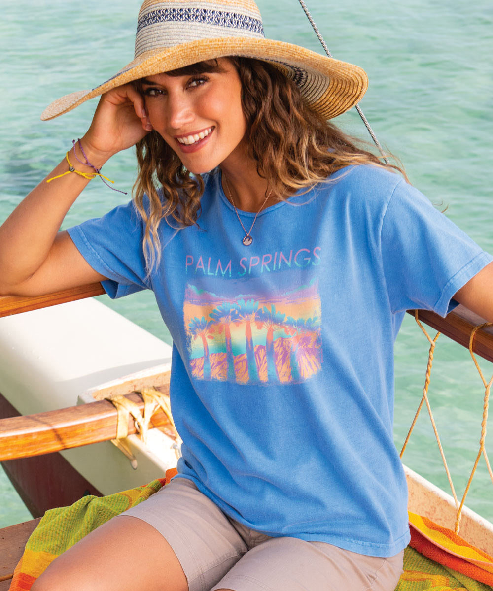 Woman wearing a blue scoop neck with a 'PALM SPRINGS' design t shirt sitting on a boat View 2