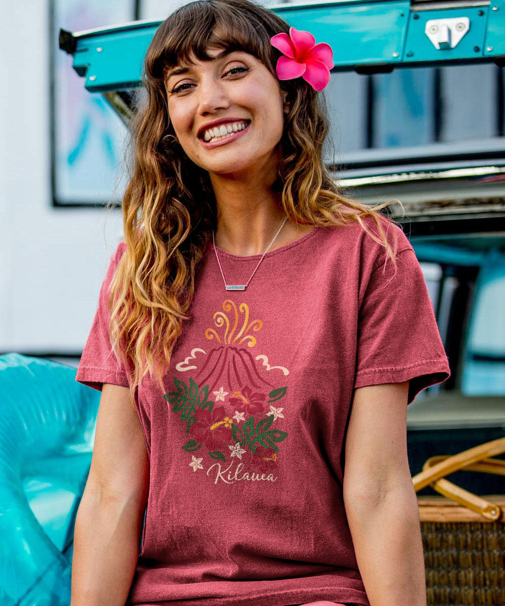 Woman wearing a red scoop neck t-shirt with a floral volcano design with the words 'KILAUEA' sitting on a vintage car View 2