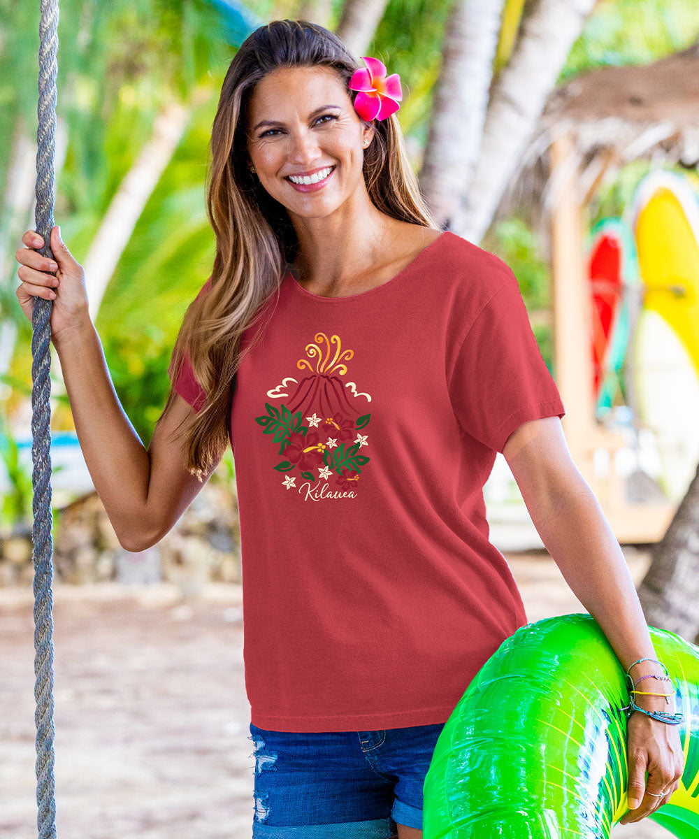 Woman wearing a red scoop neck t-shirt with a floral volcano design with the words 'KILAUEA' at a beach View 2