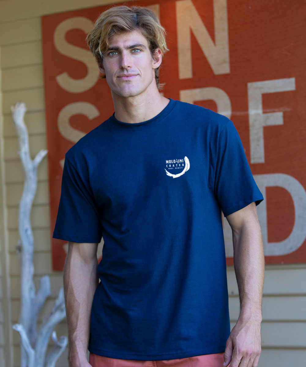 Man wearing a navy blue t-shirt with a logo in front of a red sign. View 3
