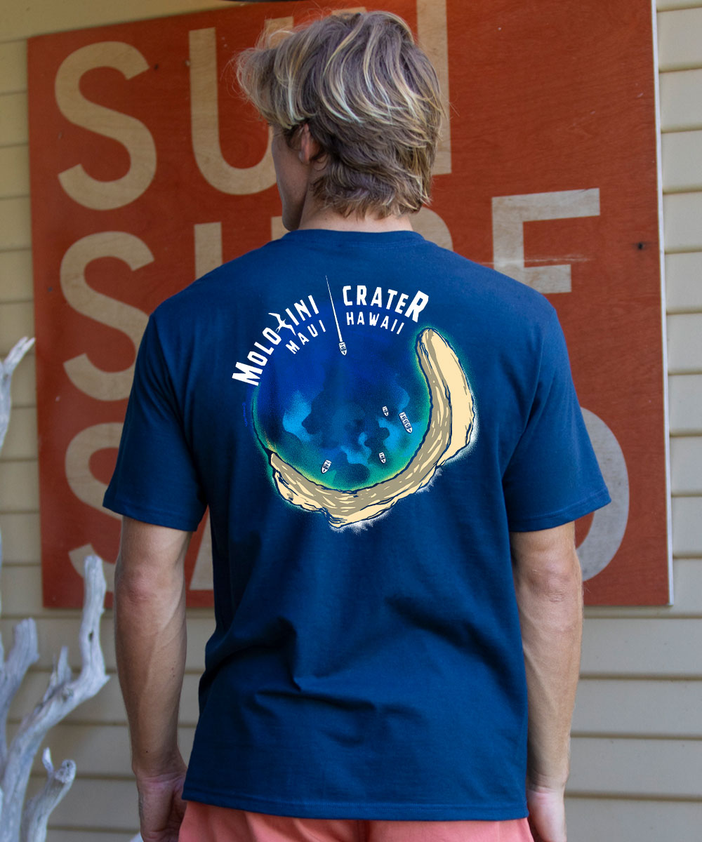 Person wearing a blue t-shirt with a graphic design and text, standing in front of a red sign. View 2