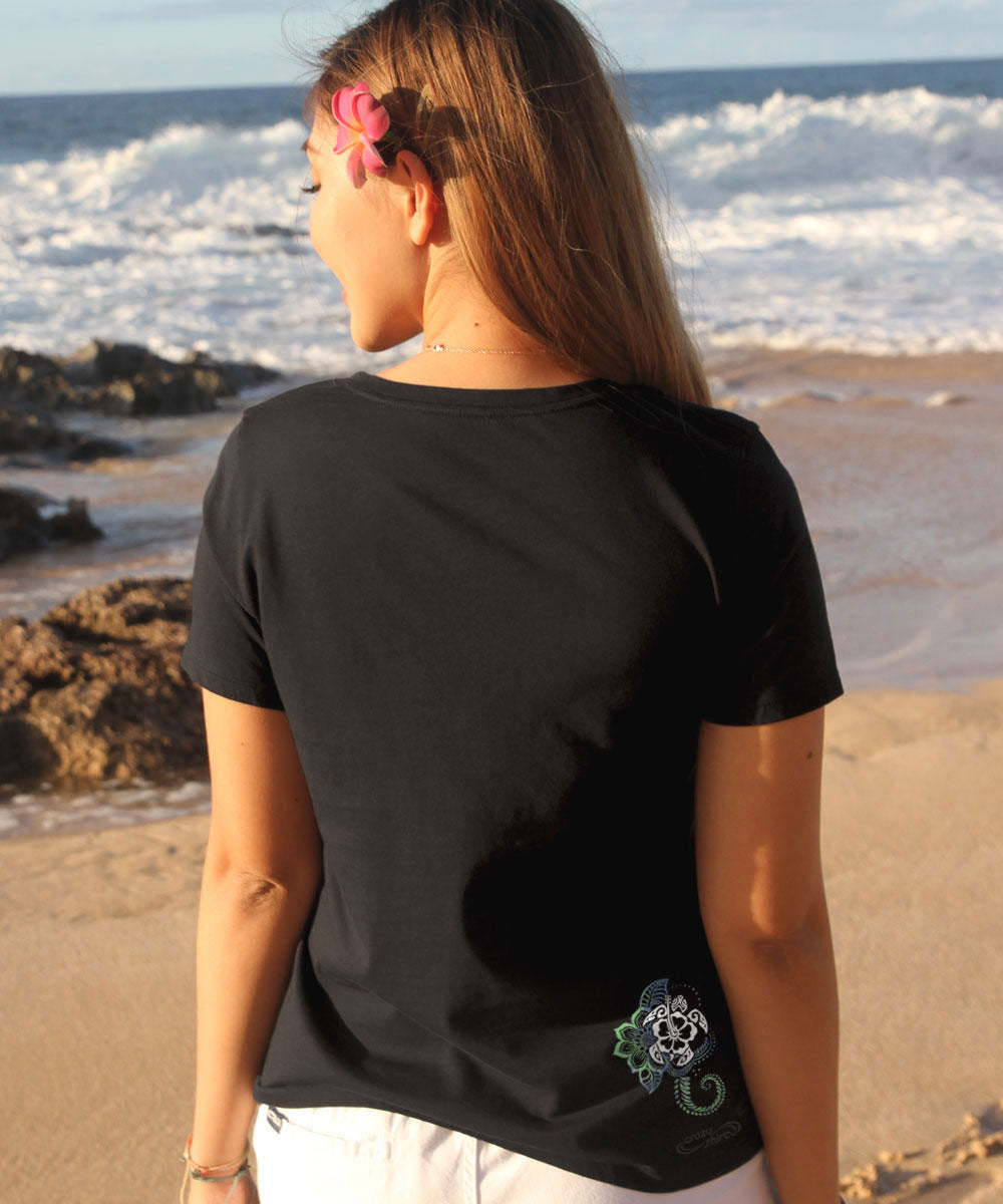 Woman standing in front of the ocean wearing a black shirt with a small design in the corner View 3
