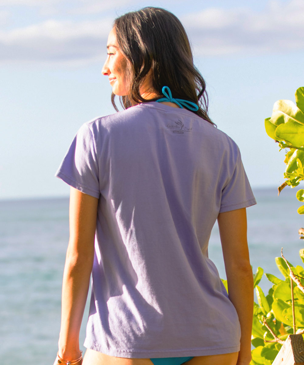 Woman wearing a purple t-shirt with a logo, standing by the ocean. View 3
