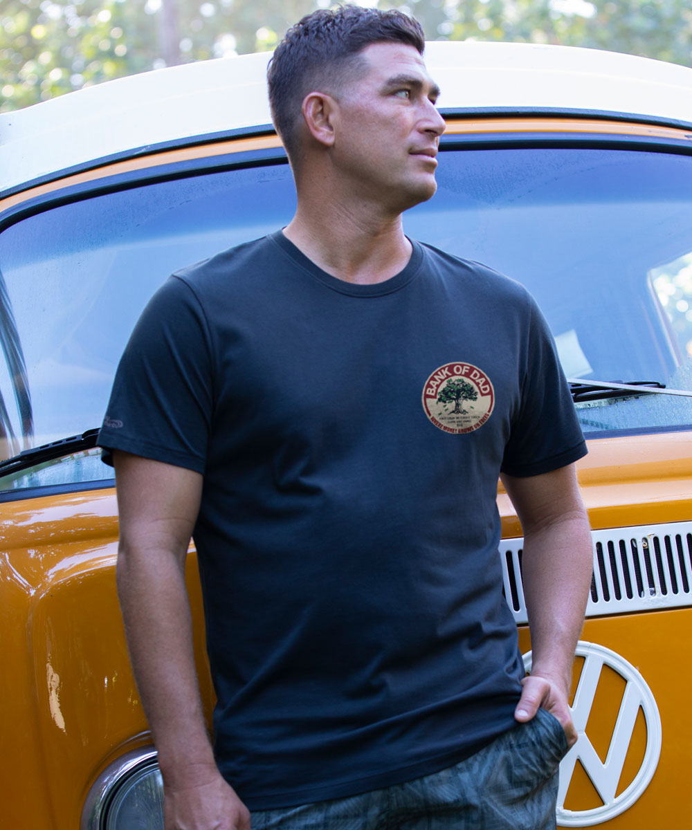 Man wearing a black t-shirt with a logo, standing next to a yellow Volkswagen van. View 3
