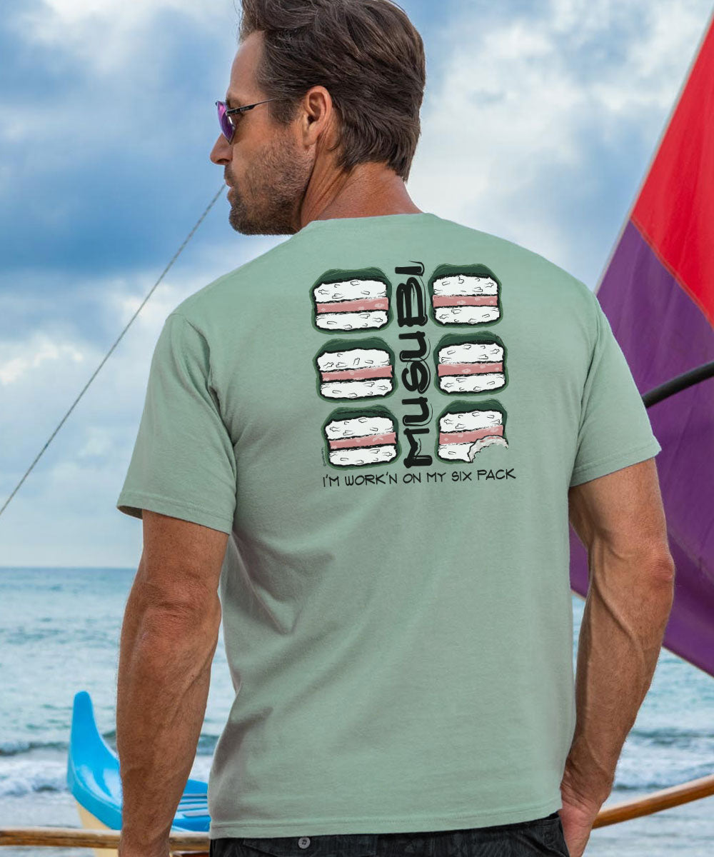A person wearing a green short sleeve crewneck t-shirt with a graphic of a musubi six pack on the back, standing near a beach setting. View 2