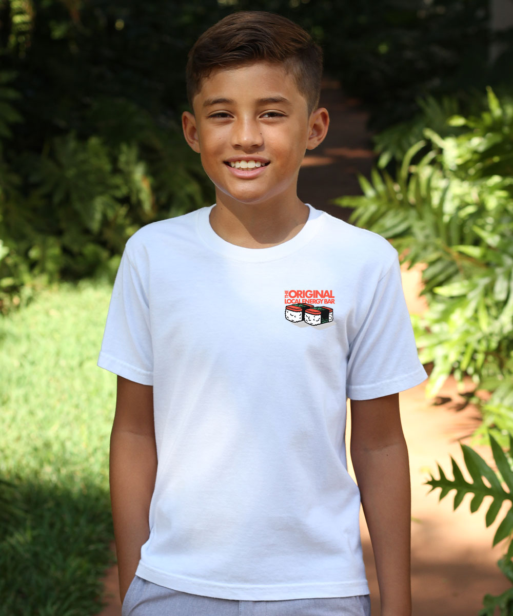 A child wearing a short sleeve crew neck t-shirt with a small spam musubi design on the front left chest area with greenery in the background. View 3