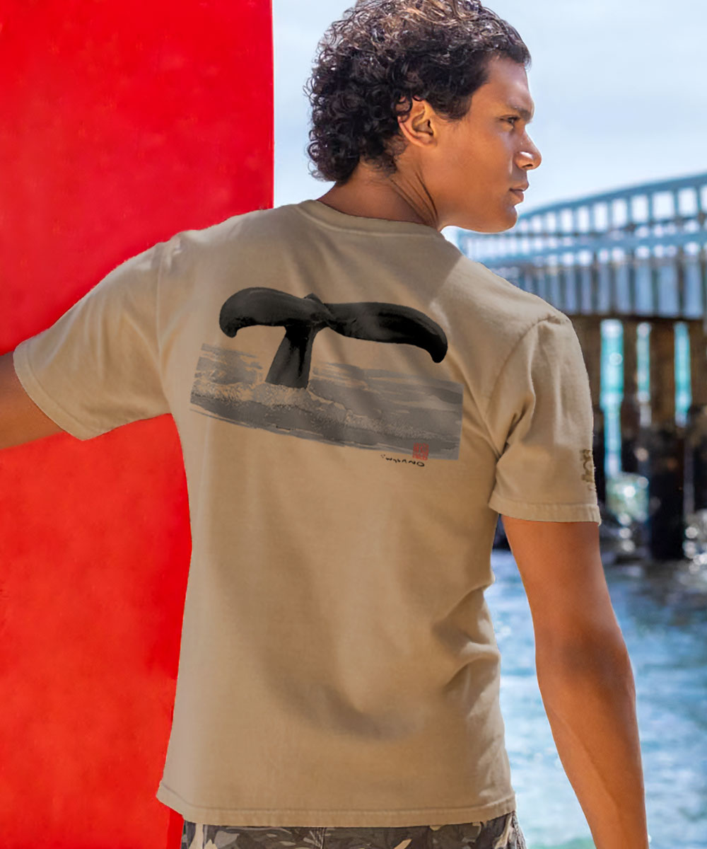 Person wearing a beige t-shirt with a breaching whale tail black graphic on the back. View 2