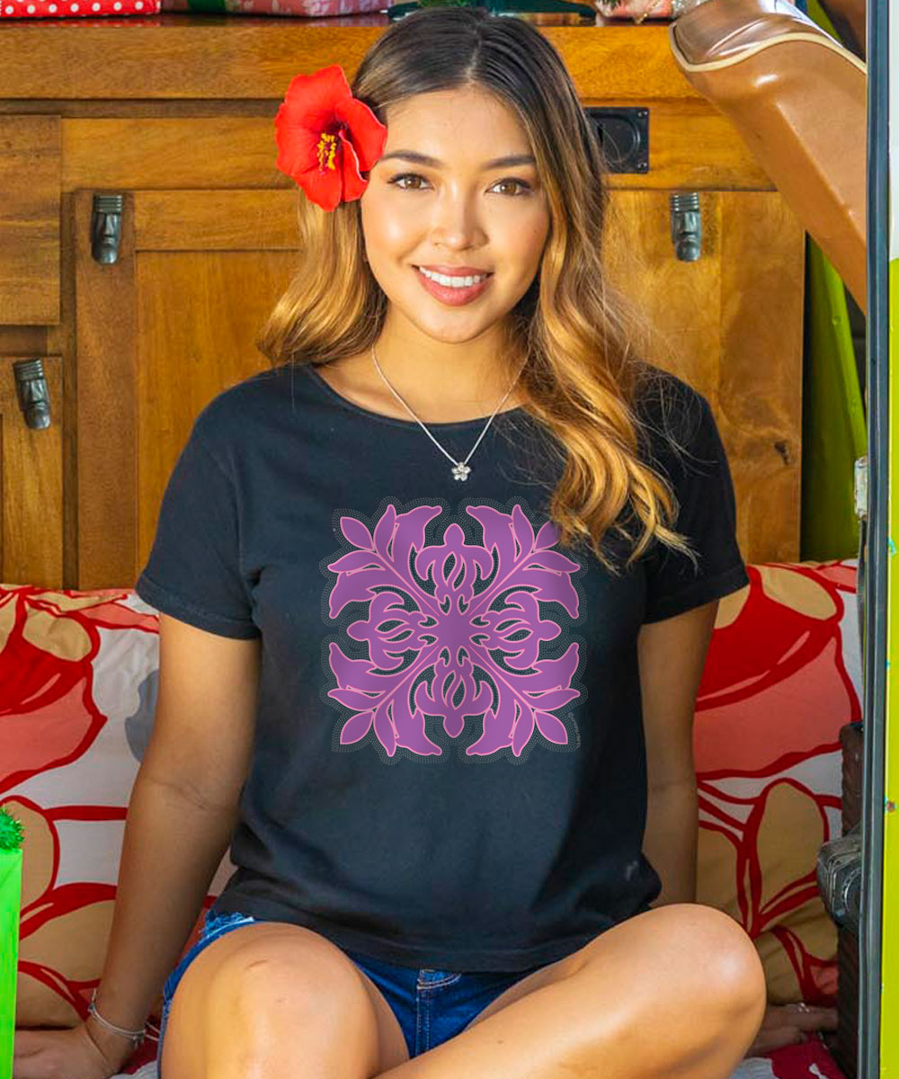 A woman wearing a black scoop neck t-shirt with a purple Quilt floral design on the center chest area, sitting in a van with decorative elements. View 2