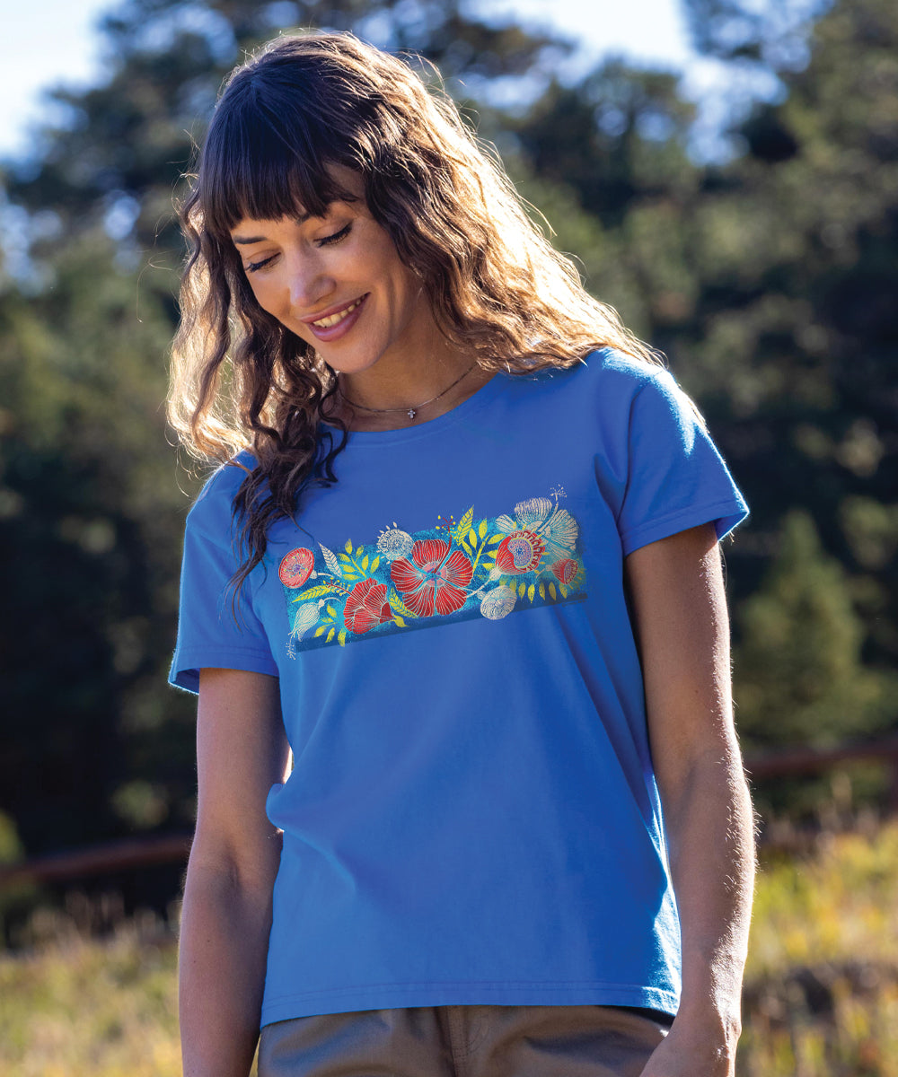 A woman wearing a blue short sleeve crewneck t-shirt with a floral design on the front, standing outdoors. View 2