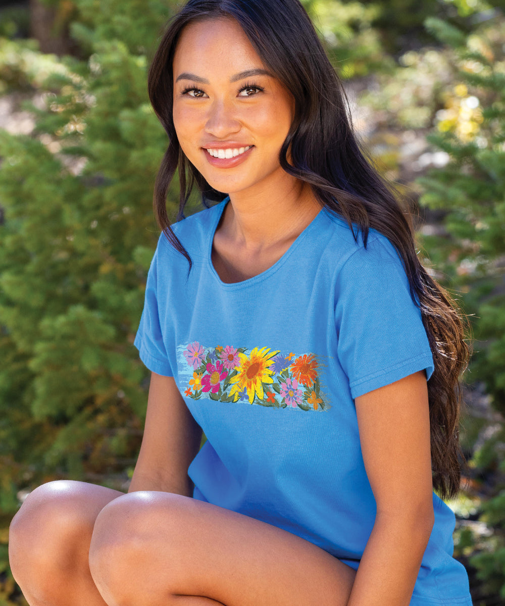 A woman wearing a blue scoop neck t-shirt with a floral sunflower band design on the front. View 2