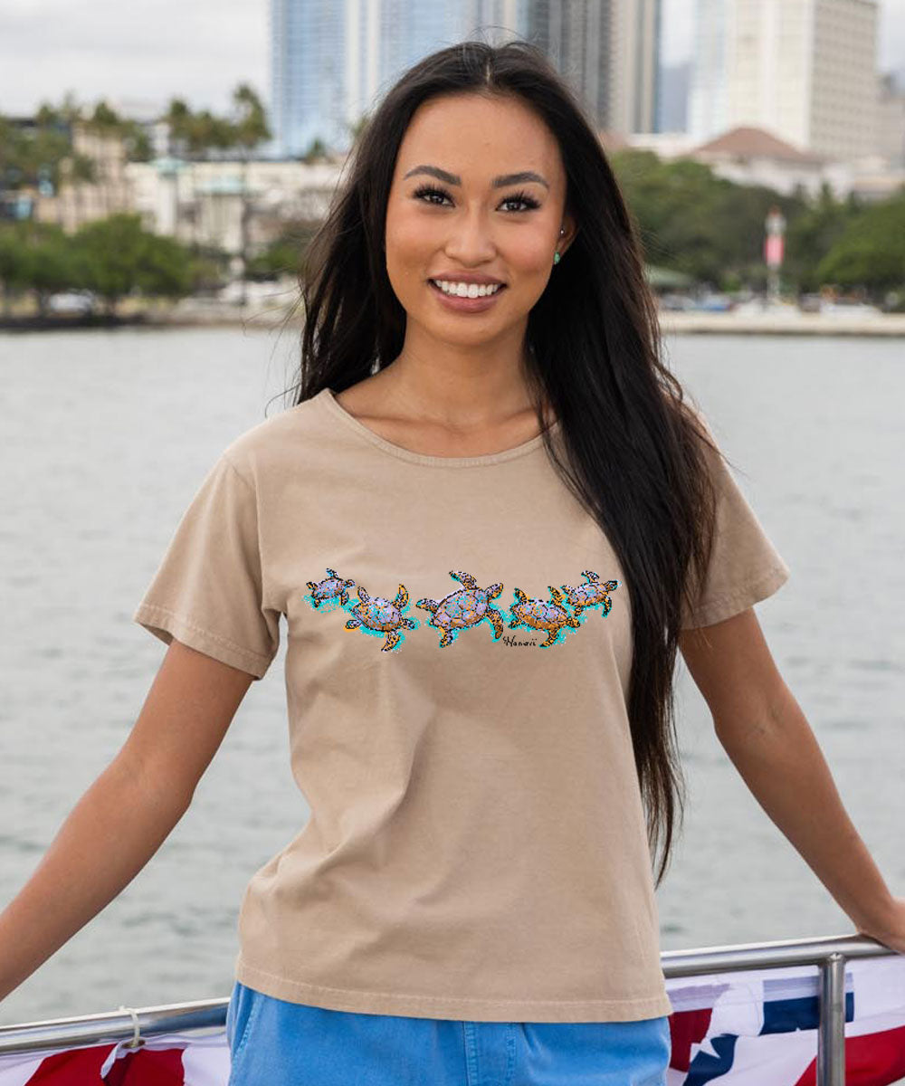 A woman wearing a beige short sleeve scoop neck t-shirt with a watercolor honu (turtle) design in a scoop neckline. View 2