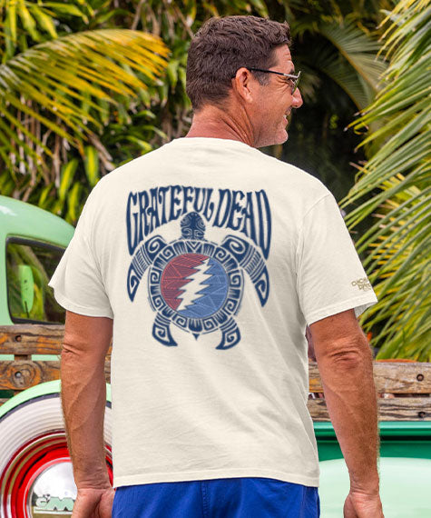 Man wearing a 'Grateful Dead' t-shirt with a turtle design, standing in front of a vintage truck and palm trees. View 2