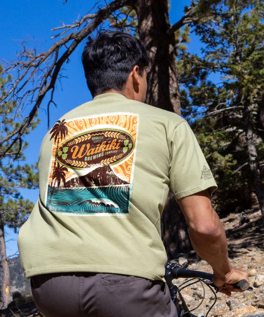 A person wearing a green short sleeve crewneck t-shirt with a graphic design on the back, standing outdoors. View 2