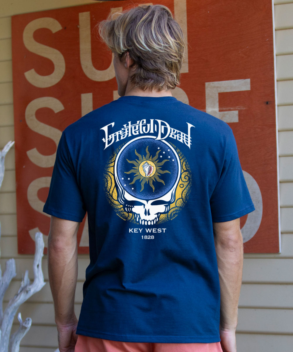 Person wearing a blue t-shirt with a Grateful Dead logo, standing in front of a sign. View 2
