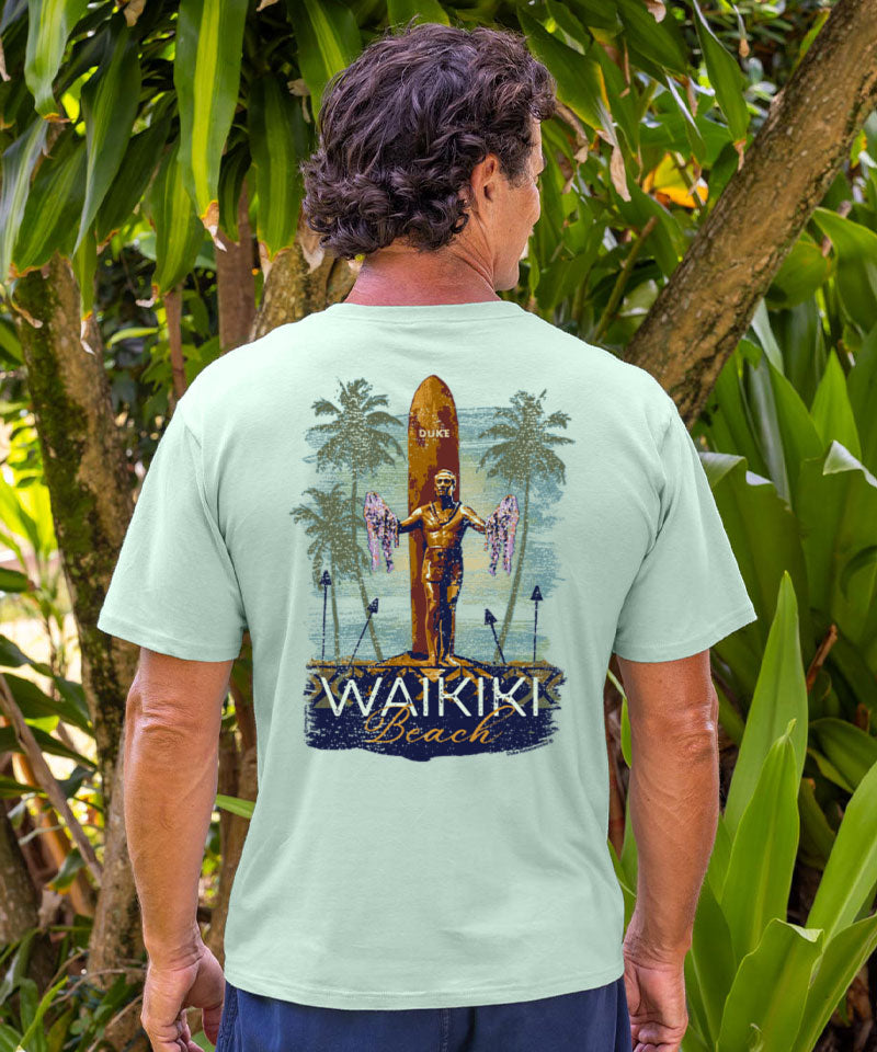 Man wearing a light green t-shirt with 'Waikiki Beach' design outdoors. View 2